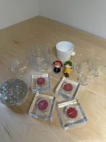 Lot arranged on a wood table, showing all items; glass tea light holders, flower frog, swan candy jar, juice glasses, bunny mug, figurines