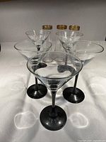 Photo showing 5 martini glasses with black stems and clear glass bowls arranged in a row.