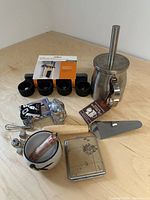 Overview of the lot on a wooden surface showing various items including the basting set, tea cup, metal case, salt and pepper shakers, playing cards, and other small items.