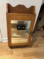 Front view of the vintage handmade pine medicine cabinet showing the mirrored door and brass knob.