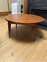 Angled front view of the round wood coffee table showcasing tapered legs and polished table top surface on hardwood floor.