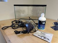 Glass aquarium tank with air pumps, tubing, and water conditioner arranged on wooden surface