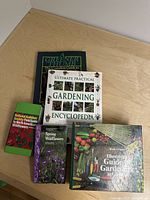 Photo of five gardening and wildflower books stacked on a wooden surface showing the titles and cover designs.