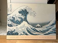 Color photo of the poster depicting a large wave with Mount Fuji in the distance, Japanese calligraphy and museum branding at bottom.