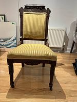 Full front view of wooden chair showing the carved wooden frame and gold upholstery on seat and backrest.