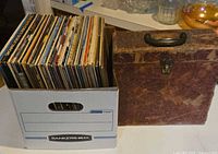 White bankers box filled with vinyl LP records next to a faux leather record case