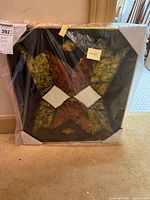 Framed batik wall art with geometric design under plastic wrap, showing full piece and close detail.