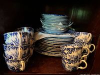 Stack of 8 blue and white transferware teacups in two stacks in front of two stacks of plates