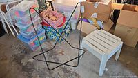 Metal butterfly chair frame next to one white plastic patio side table on concrete floor