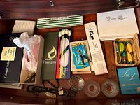 Photo showing boxed candles from Colonial Candles, Paragon, boxed cocktail utensils, Devon Lace napkins box, and a small basket of colorful cocktail spreaders.