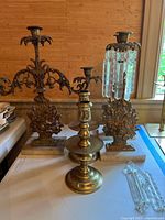 Wide view of all candlesticks on table showing both metal and brass items along with loose glass prisms.