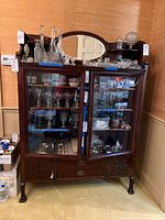 Front view of wooden china cabinet with glass doors filled with glassware, beveled mirror on top, two drawers and lower cabinet doors.