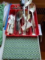 Top view of a red plastic cutlery tray containing 10 dinner knives and 4 spreaders with mother of pearl handles, silver plate serving spoons, and a lemon fork.