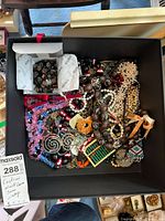 Full overview of assorted costume jewelry including necklaces and bracelets inside a black box, showing varied styles and bead colors.