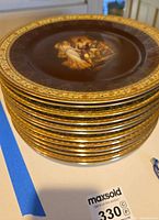 Stack of approximately 12 Czech decorative collector's plates showing dark brown color with gold and cream patterned rim.