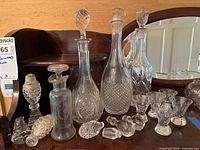 Full view of three decanters with stoppers, six small crystal glasses, and three additional decanter stoppers on wooden surface