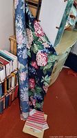 Fabric remnants with large floral pattern featuring pink and red hydrangea-like flowers and green leaves on dark blue background, draped over furniture.