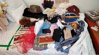 Mixed collection of hats, aprons, scarves, gloves, wallets and purses on bed