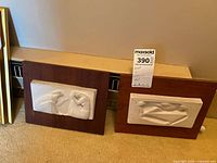 Both ceramic and wood wall arts titled 'Ruth-Naomi' and 'Bondage' side by side on the floor