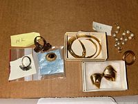 Overview of all jewelry pieces on cardboard background including earrings, button, bangles, ring, pearl bracelet, bow and circular brooches, and necklace.