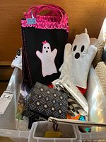 Box containing Halloween-themed trick-or-treat bags and white ghost oven mitt with pink trim.