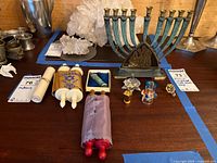Photo showing metal menorah, two miniature Torah scrolls, multiple glass dreidels, and additional Judaica items arranged on table.