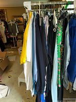 Clothes hanging on rack, showing variety of styles and colors including a yellow short-sleeve top and garments in black, blue, white, and patterned green.