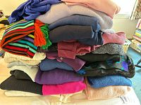 Stacked pile of women's sweaters in assorted colors and patterns including stripes, floral, purples, blues, black, and cream.