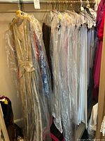 Image of a rack of vintage dresses mostly white and pastel colors covered in clear garment bags.
