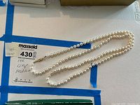 Full view of pearl necklace laid flat on white surface with MaxSold label showing note ‘14K clasp’