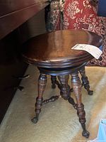 Wood piano stool with round seat and metal claw-style feet next to a piano and a patterned rug.