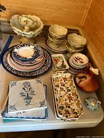 Full lot overview showing multiple ceramic and pottery items including trivets, dishes, plates, jug, and pottery bowl, arranged on a table.