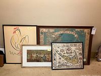 Four framed art pieces on a floor against wall, including two Nantucket maps, Picasso print, and group dining scene print.