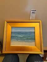 Frontal view of the framed oil painting showing beach scene with waves in a gold frame