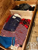 Overview image of vintage clothing lot including sweaters, shirts, and knitted items in a wooden box.