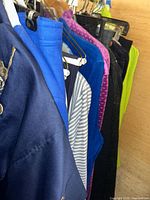 Photo showing a close-up view of various sweaters and tops in blue, purple, grey striped, and lime green colors hanging on a rack
