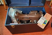 Vintage Domestic brown textured sewing machine in blue-lined case, with power cord and additional parts visible inside the case.