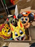 Photo showing a box containing five vintage Halloween masks including a Mickey Mouse mask and animal faces such as a lion, cat, bunny, and another animal.