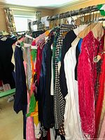 Full rack of assorted vintage ladies clothing featuring dresses, blouses, and vests in varied styles and colors hanging on a clothing rack.