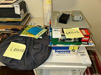 Photo of various Lego items placed on a table including a grey baseplate, black and white bricks, and a Lego box with more bricks inside.