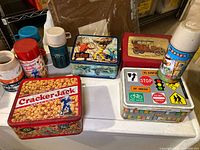 Overview photo of four vintage metal lunch boxes and three thermos bottles on table, showing condition and contents.