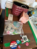 Photo showing bin holding bag of various vintage political buttons, with some scattered on table including 'Humphrey For President' button and others.
