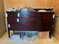 Front view of the vintage wooden side board cabinet with three drawers and two side doors, showing brass handles, scratches and scuffs on wood surface. Contents on top and below not included.