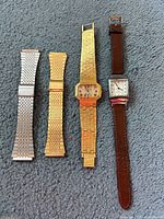 Four vintage watches and two metal bracelet bands displayed on carpet.