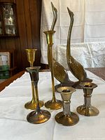 Set of five vintage brass candle holders of varying sizes and styles, showing patina and signs of use.
