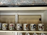 Six flower-themed cups lined up on a shelf, each with a different colored floral design.