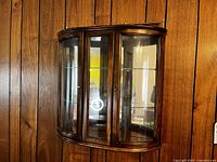 Front and side angled view of vintage curved glass display cabinet showing wood frame, glass doors, and shelves inside.