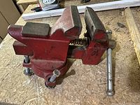 Side angle photo showing red workshop bench vise with metal handle and jaws.