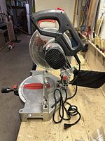 Front angle of Craftsman mitre saw showing handle with red accents, saw blade, and adjustable metal base with angle markings.