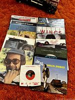 Full view of 14 mixed genre vinyl records arranged in a stack on carpet including Elton John and Waylon Jennings albums.